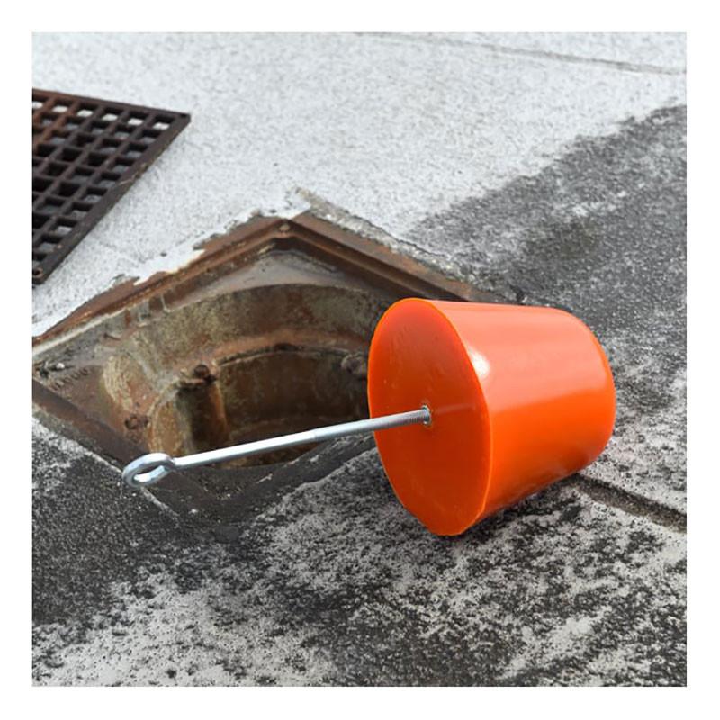 The UltraTech Drain Plug 211, a large orange tool crucial for preventing chemical spills, is positioned near an open industrial gutter drain on a flat rooftop. The plug, attached to a long metal handle, stands ready as the area shows wear from previous spill responses.