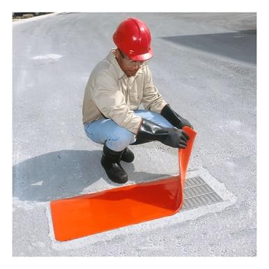 Wearing protective gear, including a red helmet, beige shirt, black gloves, and boots, a person is expertly squatting on the pavement to place an UltraTech Drain Seal from UltraTech International over a drain as part of an emergency response to improve stormwater management.