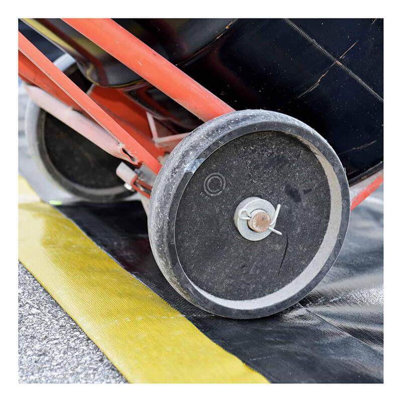 The UltraTech dolly, with two black wheels, transports a large black container. Its red frame moves across a yellow and black striped surface, possibly for spill containment or with an UltraTech Ultra-Containment Berm Economy PE Model 824_ for added safety.