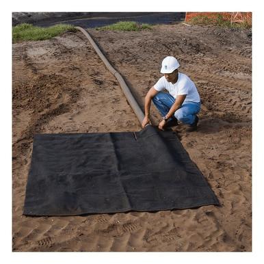 A person in a white hard hat and T-shirt kneels on a sandy surface, carefully laying out an UltraTech Dewatering Bag 972_-OS for storm water pollution prevention. A long hose runs in the background, with contrasting orange netting and patches of grass in the distance.