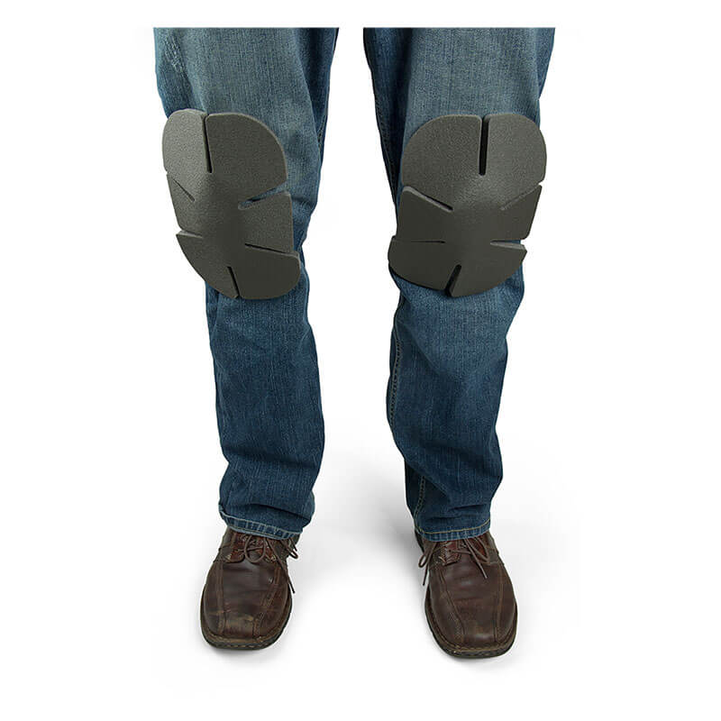 A person wearing blue jeans with Working Concepts Soft Knees Disposable Knee Pads 1012 and brown shoes. The gray knee pads, designed by Working Concepts, feature multiple sections for ultimate flexibility. The image highlights the lower legs, emphasizing the area from the knees downward.