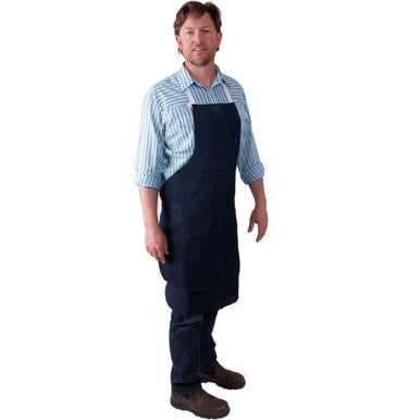 A man wearing a striped shirt and the MCR Safety Denim Apron stands against a white background. He has short hair and is dressed in dark pants and brown shoes, embodying a classic workwear style.