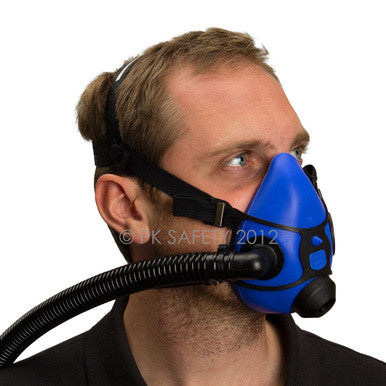 A person is wearing the Allegro Half Mask Constant Flow Airline Respirator 9920 from PK Safety Supply. The silicone blue facepiece, secured by elastic straps around their head, covers their nose and mouth with an attached black hose. They are looking to the side, ensuring continuous airflow.