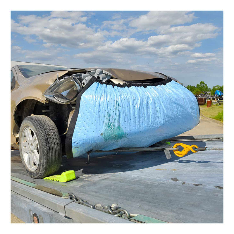 A dismantled car with a deflated airbag protruding from the front is secured on a flatbed truck. UltraTech Spill Diaper 0275, from UltraTech International, Inc, surrounds the vehicle to emphasize environmental protection. The front bumper is removed, exposing the airbag, while the sky and some trees are visible in the background.