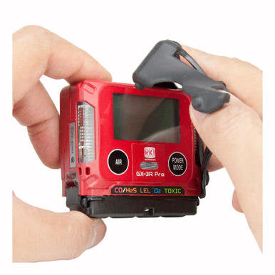 A person holding an RKI GX-3R Pro Gas Confined Space Monitor with a red casing and a digital display. The device features buttons labeled "Air" and "Power Mode," and the screen showcases various gas indicators, including CO, H2S, LEL, and O2. It is equipped with wireless communication for seamless Bluetooth data sharing.