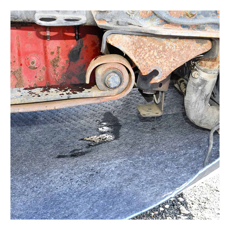 A close-up view features a rusty car part with a hole in the absorbent material beneath it. This worn and stained UltraTech Spill Diaper 0275, from UltraTech International, Inc., is placed on a surface littered with small pebbles and debris, emphasizing the crucial role of spill containment in ensuring effective environmental protection.