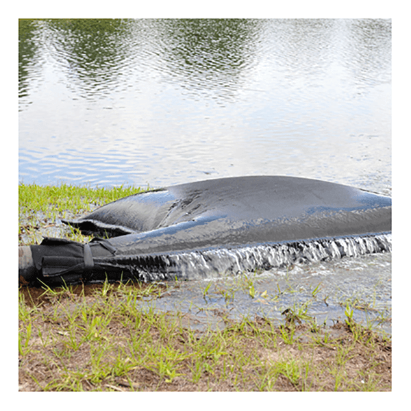 An UltraTech Dewatering Bag 972_-OS by UltraTech sits near a pond’s edge, releasing filtered water onto grass—an effective solution for stormwater pollution prevention. Trees reflect in the pond behind it.
