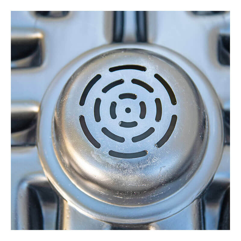 A close-up view of a metallic stovetop burner cover showcases a circular, concentric geometric pattern of holes. Its slightly worn, reflective surface brings to mind the UltraTech IBC Funnel 0648 from UltraTech International, Inc. Parts of the stove's grates can be seen in the background, enhancing the industrial aesthetic.