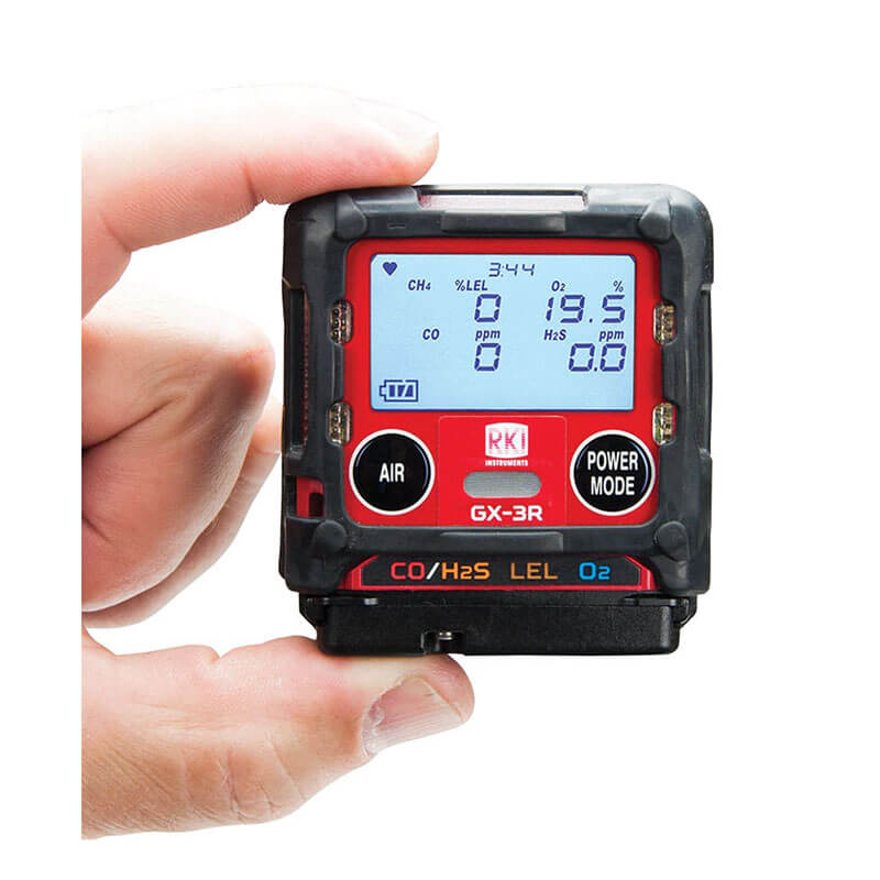 A hand holds an RKI Instruments GX-3R 4 Gas Confined Space Monitor 72-RA-C, displaying CO, H2S, LEL, and O2 levels with visible "AIR" and "POWER MODE" buttons—a reliable monitor for confined spaces.