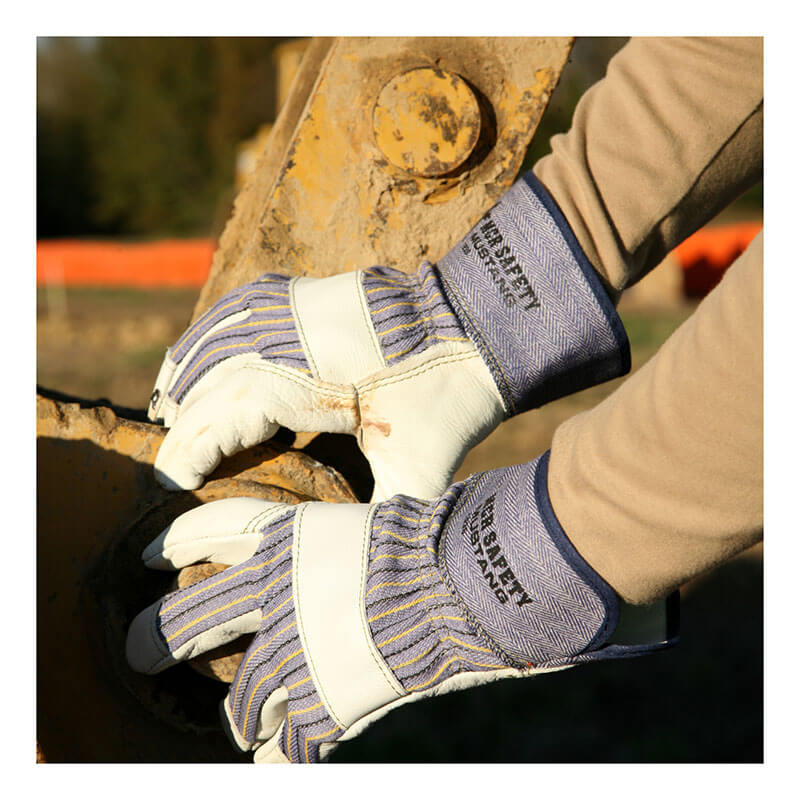 Wearing MCR Safety's Mustang Grain Leather Palm Gloves 1935, a person grips a large rusted metal part while operating heavy outdoor machinery.