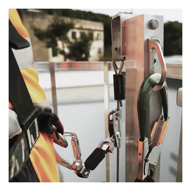 Wearing safety gear, a person uses the Frontline Ladder Cable Vertical Lifeline System VLCS by Frontline Fall Protection to secure themselves to a rooftop anchor point, highlighting reliable fall protection.