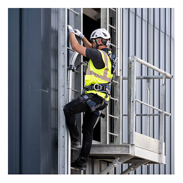 Wearing PPE, a worker climbs a roof access ladder equipped with the Frontline Securail Pro Vertical Lifeline System VLRS by Frontline Fall Protection on a building's exterior next to a platform.