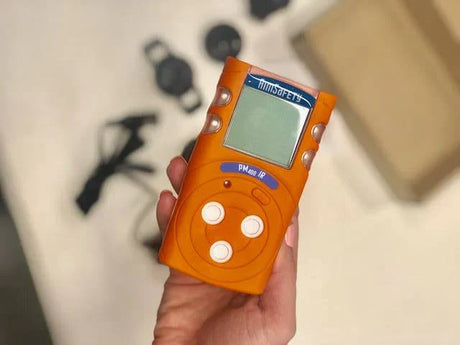 Hand holding orange gas detector with digital display. 