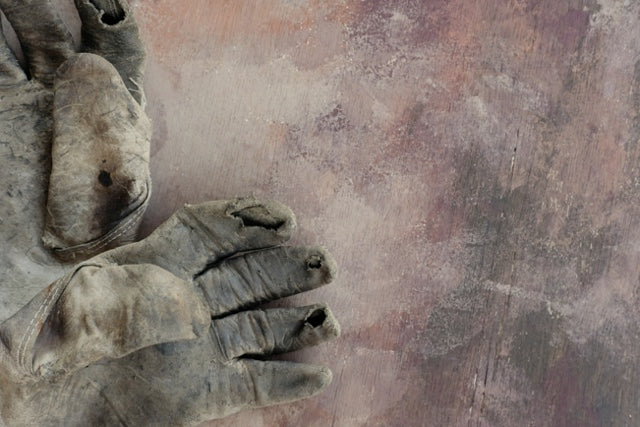 Visible signs of wear and tear on a worker's safety gloves includes holes and rips.