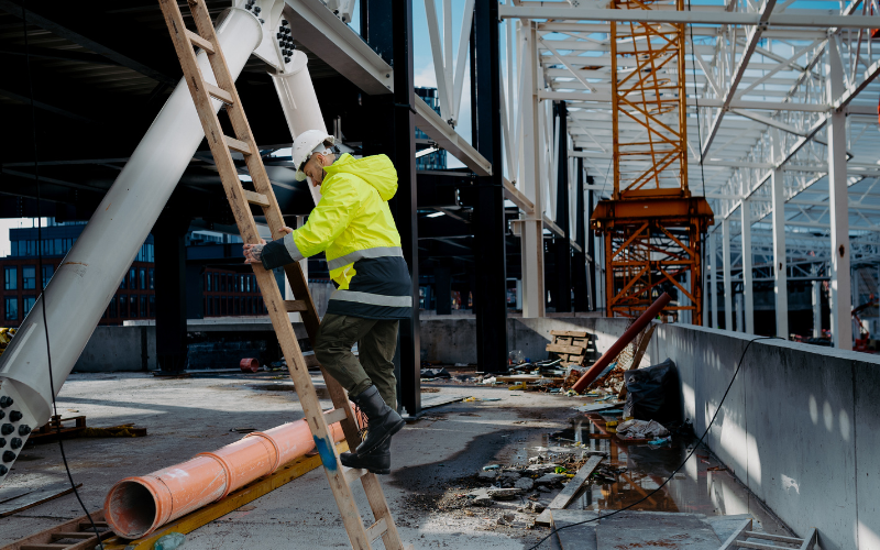 Construction worker climbing on a ladder in a construction site.