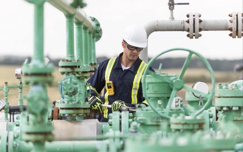Worker working on gas pipes while wearing gas monitor clipped to chest.