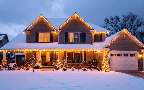 House decorated with Christmas lights in winter with snow on ground.