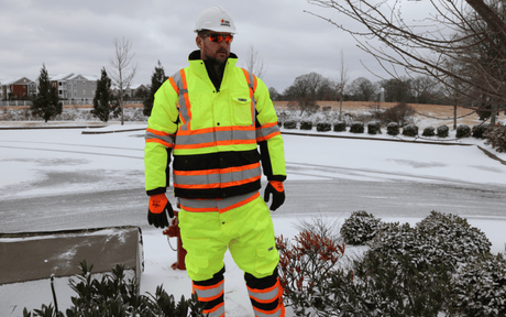 Man standing in snow wearing hi-vis workwear, hard hat, and red safety glasses.