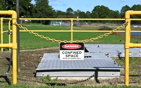 Danger confined space sign hangs on yellow chair blocking off manhole.