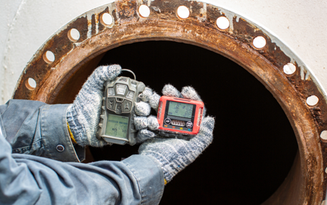 Worker holds gas detection devices in front of confined space manhole stainless tank.