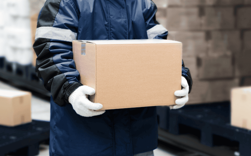 Worker in warm jacket and thick gloves, carrying a box.