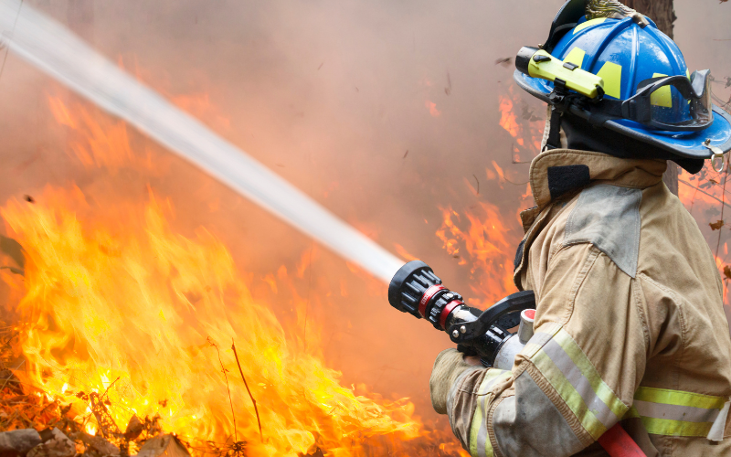 Firefighte putting out fire with water shooting out of hose.