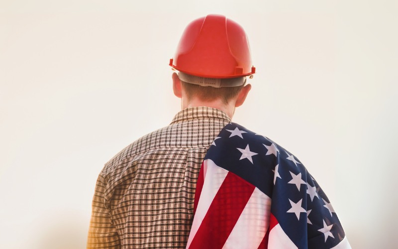 Worker wearing red hard hat with US flag draped over his shoulder.
