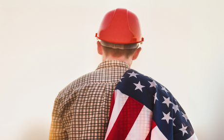 Worker wearing red hard hat with US flag draped over his shoulder.