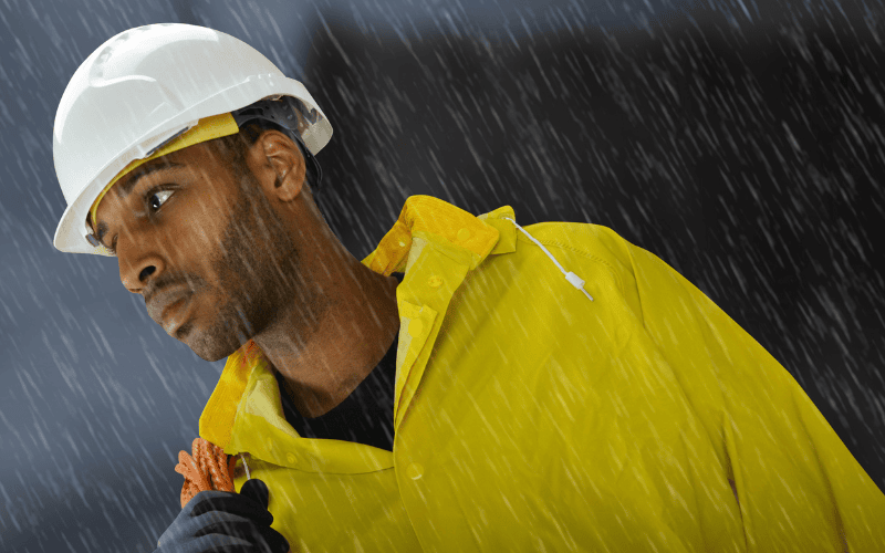 Worker wearing yellow rain jacket and hard hat standing in the rain.