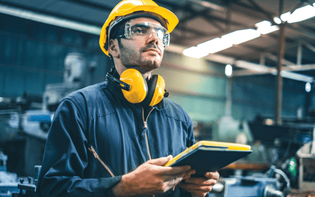 Person in a factory setting wearing safety gear and holding a tablet.