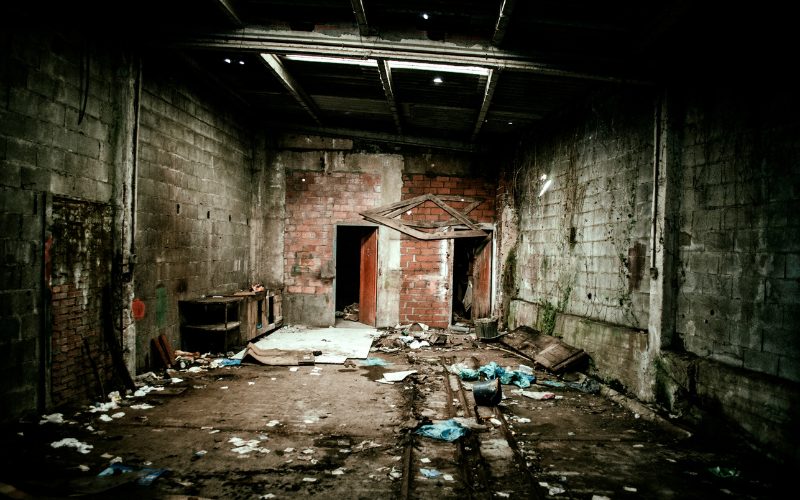 Abandoned room of building with debris on ground.
