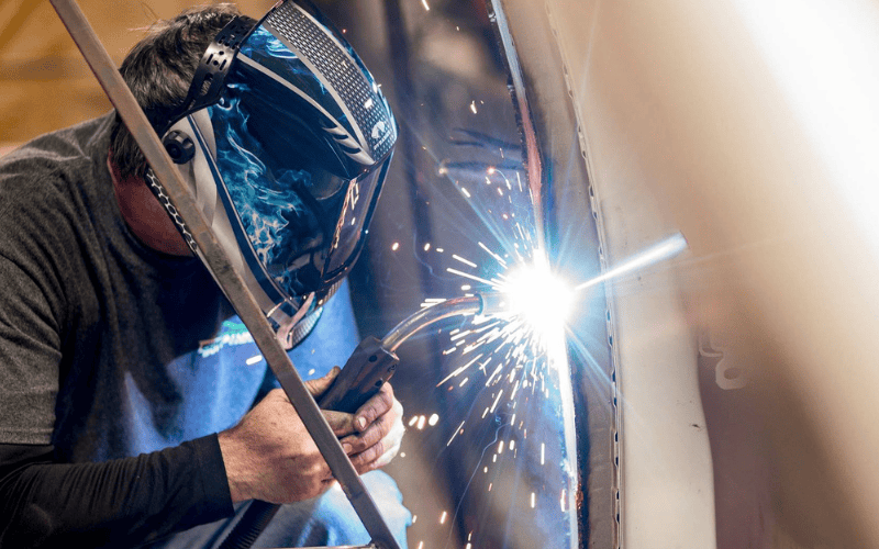 Person wearing welding helmet and welding with sparks flying.