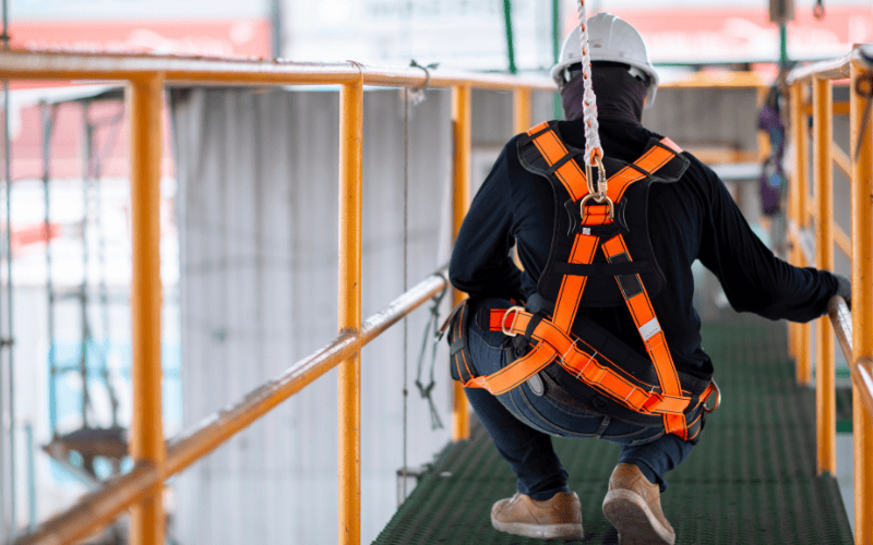 Worker wearing fall protection PPE and harness kneeling down on platform in construction site.