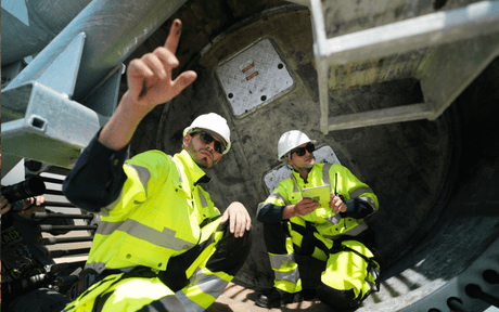 Construction workers in high-visibility gear inspect large industrial machinery.