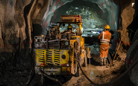Workers operate mining equipment in underground tunnel excavation.