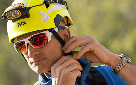 Man buckling strap of yellow Petzl helmet, wearing head lamp attachment and glasses.
