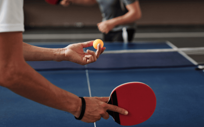 Man holding ping pong ball and paddle about to serve.
