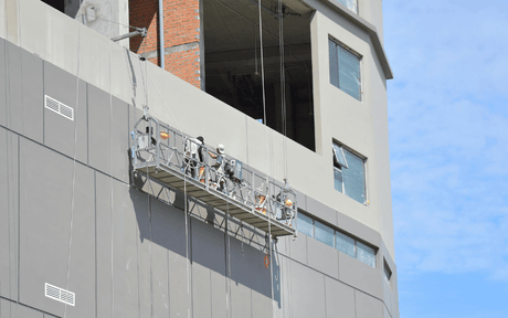 Worker on suspended scaffolding on a high-rise building against a blue sky