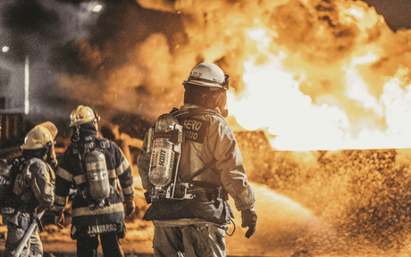 Firefighters in protective gear walking towards a large fire.