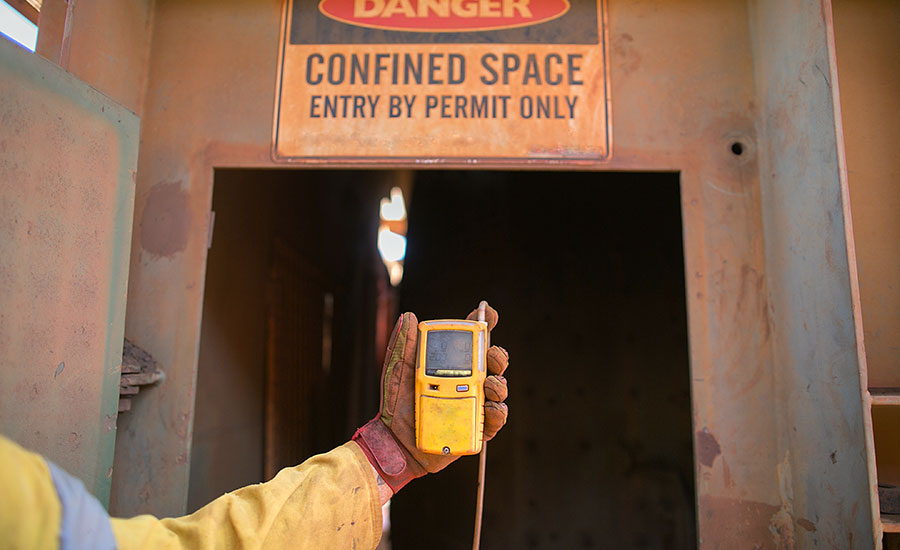 Worker holds a portable gas detector before entering a confined space.