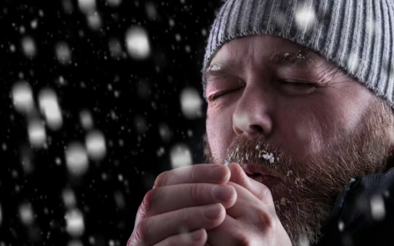 Worker in the snow breathing into clasped hands.