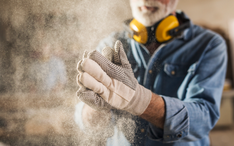 Worker clapping hands together to get dust off work gloves.