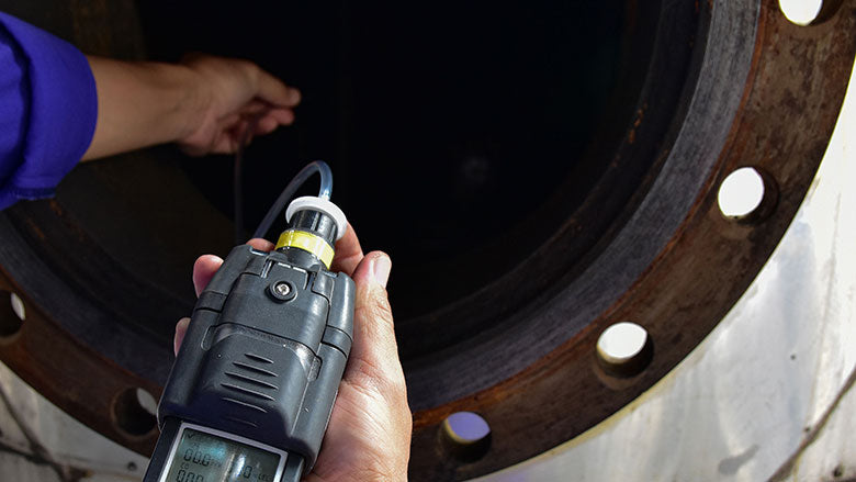 Worker testing a confined space for hazardous gases.