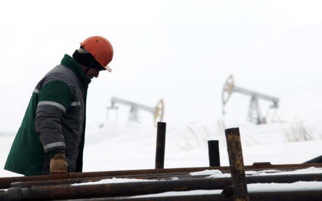 Worker outside in the cold with oil drills in the background.