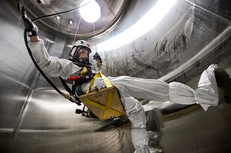 Worker wearing hazmat suit, full-face respirator and other PPE lowers themselves down a confined space.
