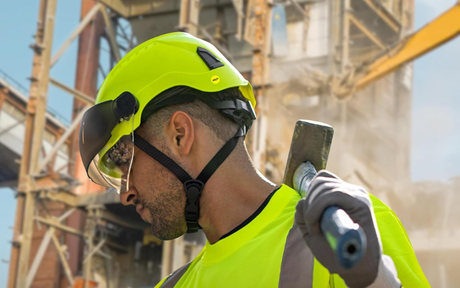 Worker wearing PIP Traverse Vented Industrial Climbing Helmet holding a tool while working at a construction site.