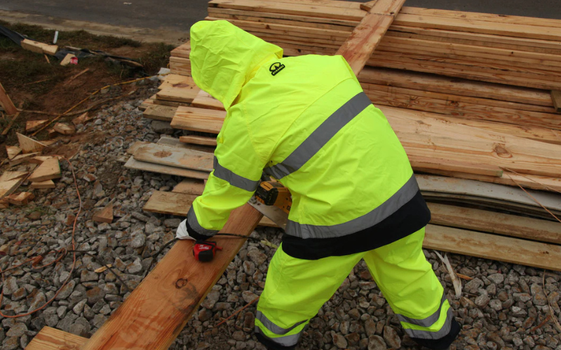 Worker wears Pyramex hi-vis workwear while cutting wood in cold, rainy weather.