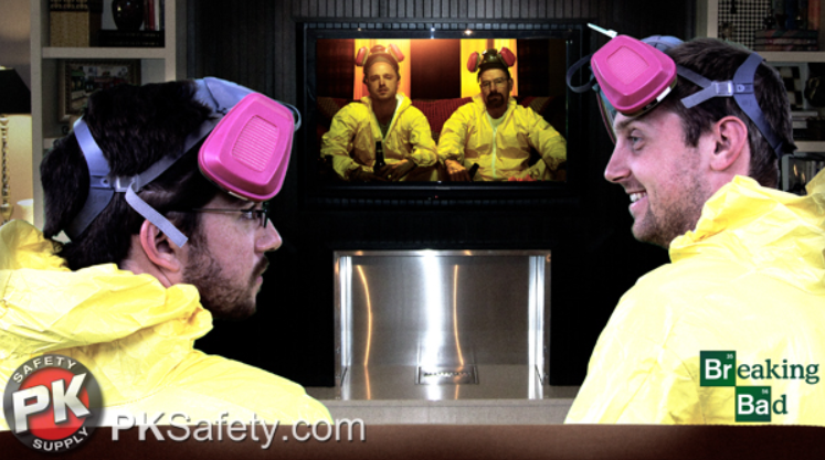 Two guys dressed in hazmat suits with respirators on their heads watch tv.