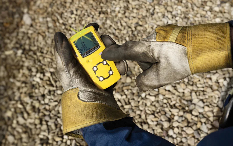 Worker using handheld gas detector device on gravel-covered site