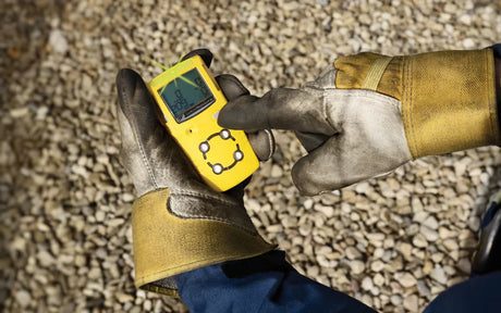 Worker using handheld gas detector device on gravel-covered site